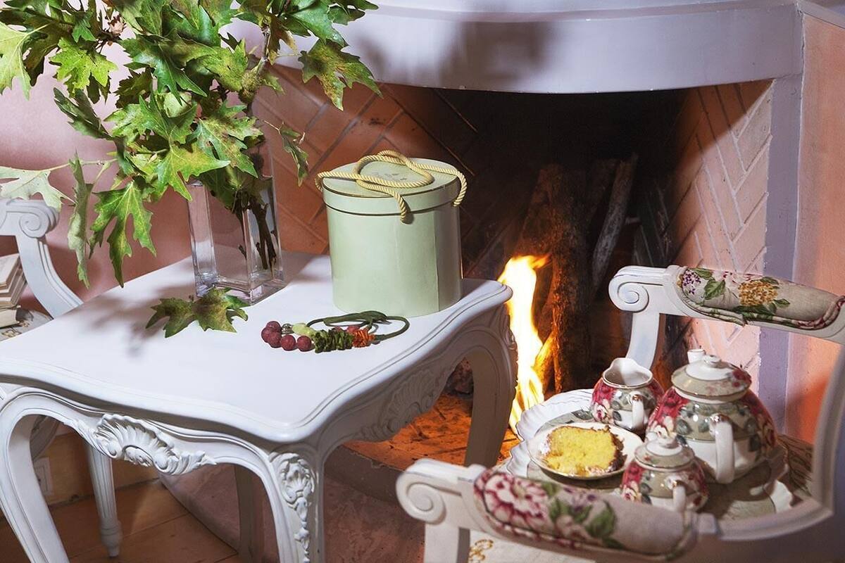 A cozy room with a fireplace, a table with a vase of green leaves, and a tea set.