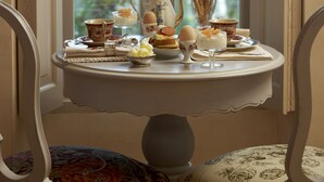 Una mesa servida con té y pasteles junto a una ventana que da a una casa.