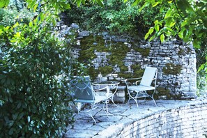 Un mur de pierres recouvert de mousse, deux chaises en métal et une table, le tout dans un décor de jardin.