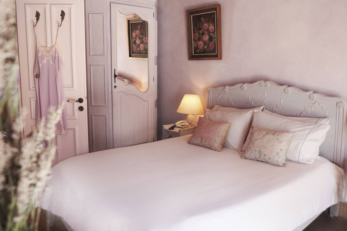 A bedroom with a large bed, a nightstand with a lamp, a telephone, and floral wall art.