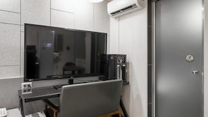 Un espacio de oficina moderno con una pantalla plana grande, una computadora de escritorio y una silla. Hay un equipo de aire acondicionado en la pared y una puerta cerrada con cerradura.