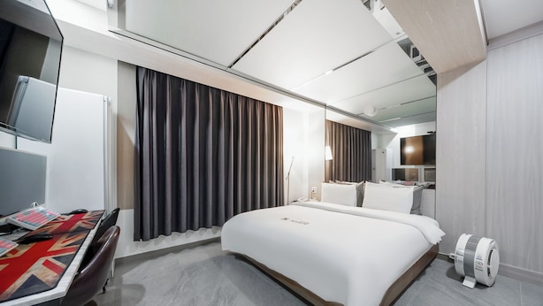 Una habitación de hotel moderna con una cama grande, un escritorio con mantel de la bandera del Reino Unido, un televisor de pantalla plana y un ventilador de pie.