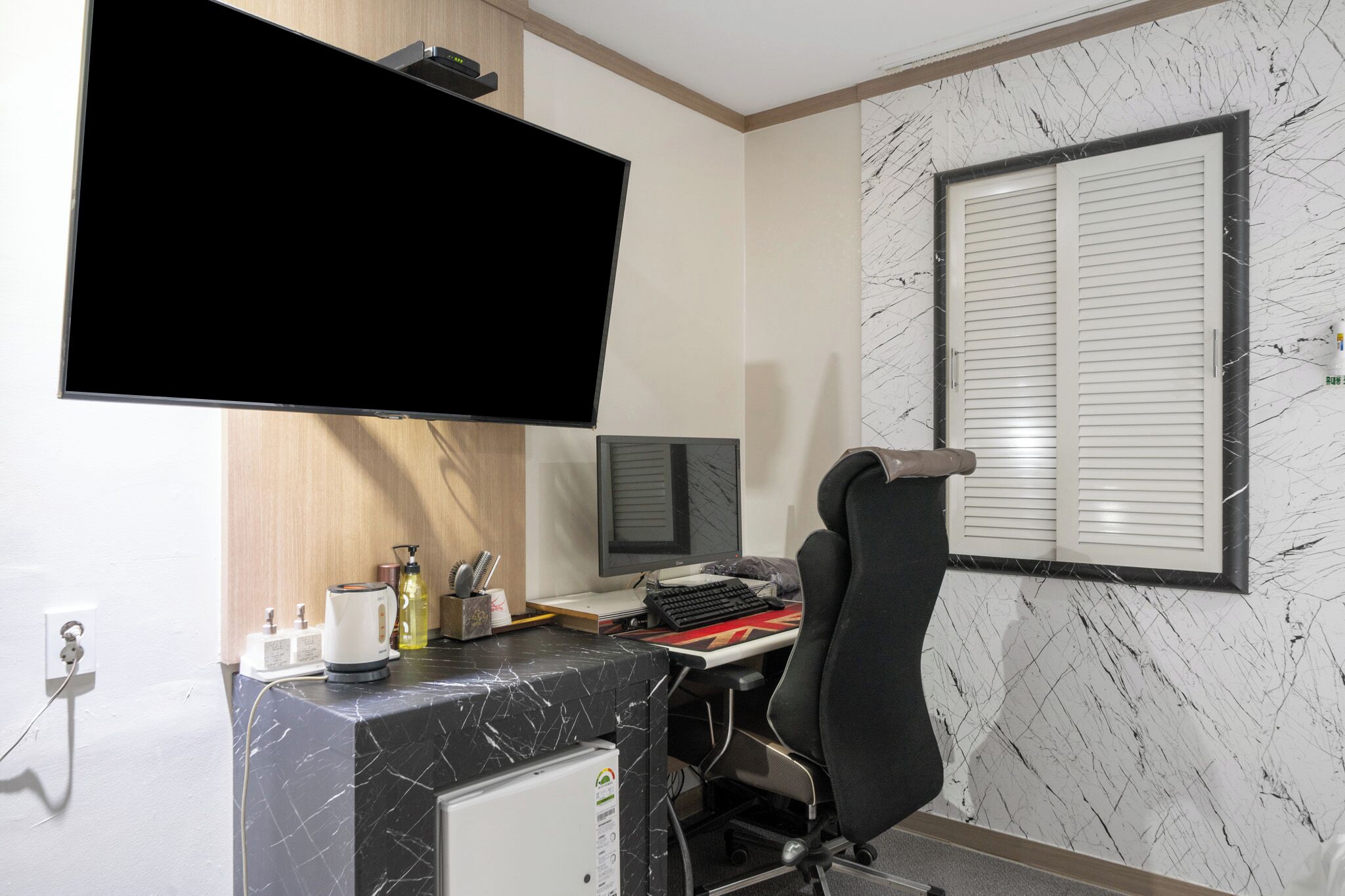 Un espacio de oficina moderno con una televisión de pantalla plana, una computadora, una silla y un ventanal con persianas.