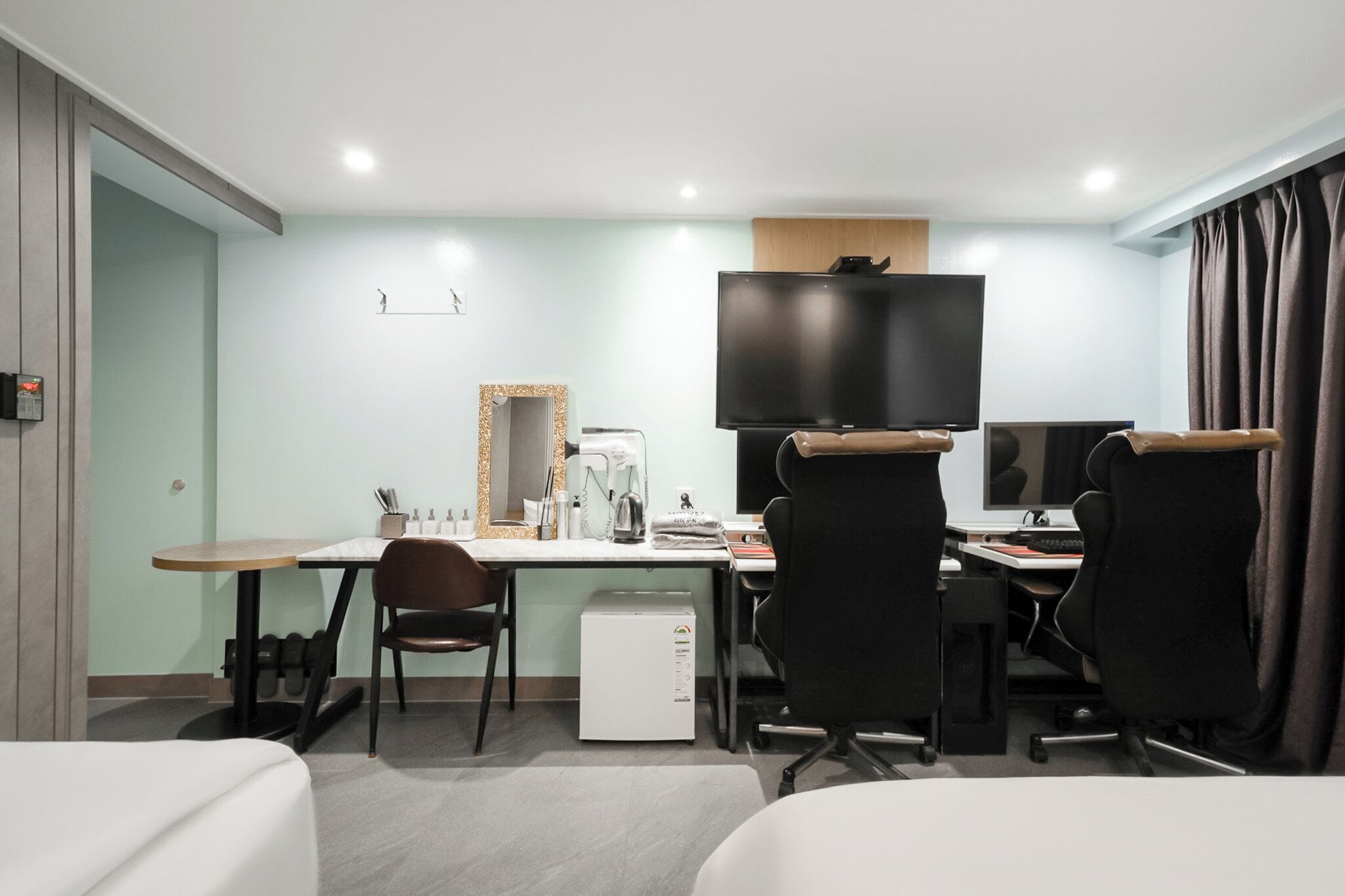 Una habitación de hotel con escritorio, dos sillas, televisión, refrigerador pequeño y cama.
