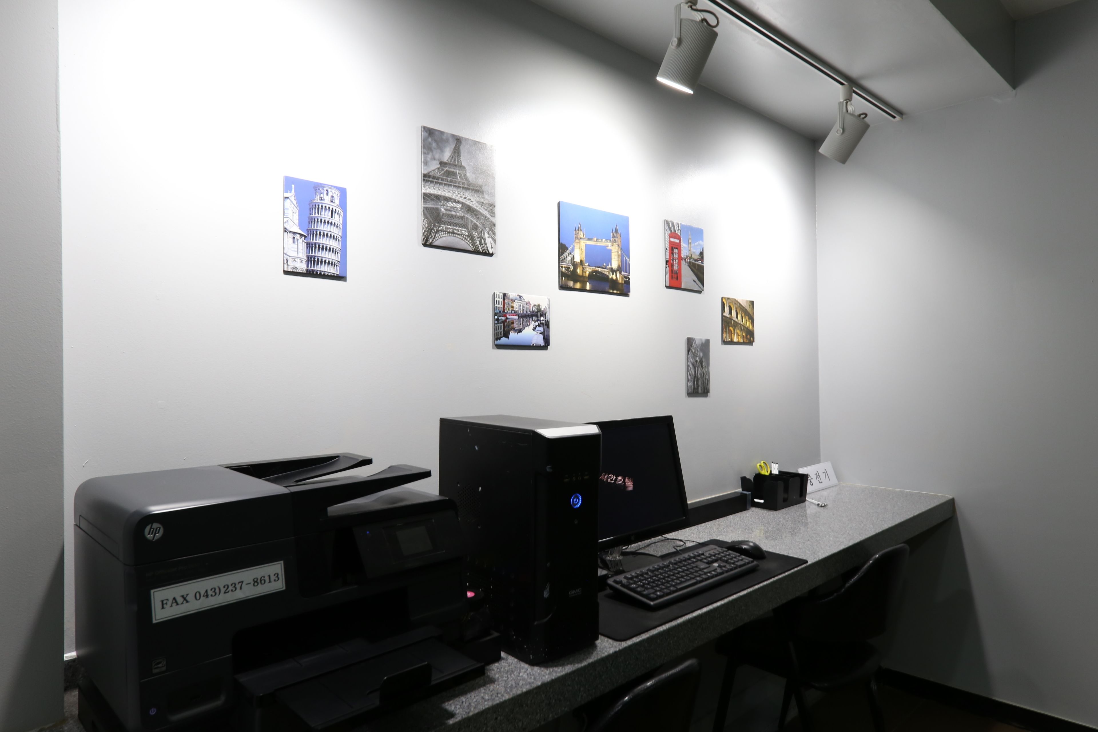 A workspace with a desktop computer, printer, and a wall with framed pictures.