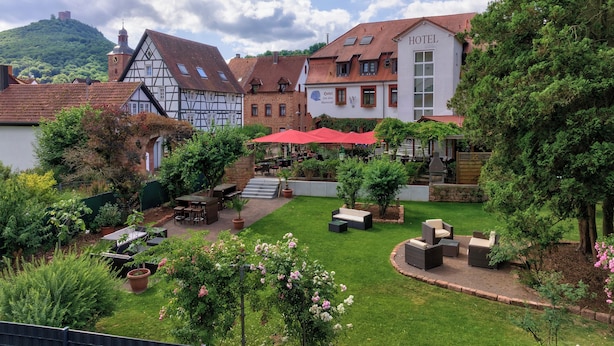 A hotel with a courtyard featuring outdoor seating, a garden with flowering plants, and traditional architecture. - Zum Alten Wasserrad - L Antica Ruota (Annweiler am Trifels)