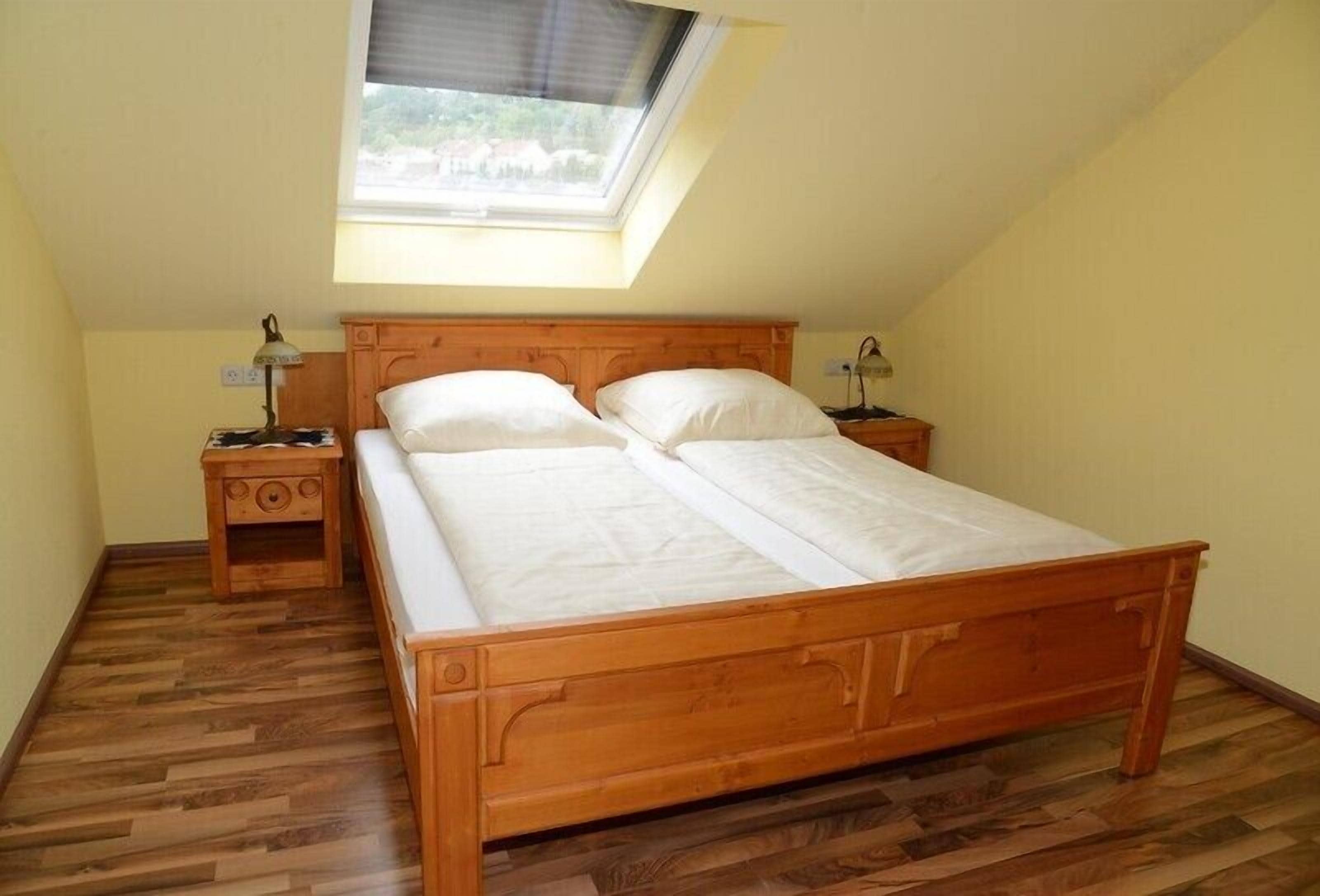 A bedroom with a wooden bed, two bedside tables, a skylight, and a wooden floor.
