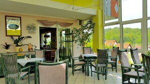 A dining area with green and beige chairs, a table with a white tablecloth, and a view of greenery outside. - Hotel-Pension Haus Hubertus (Weigendorf)