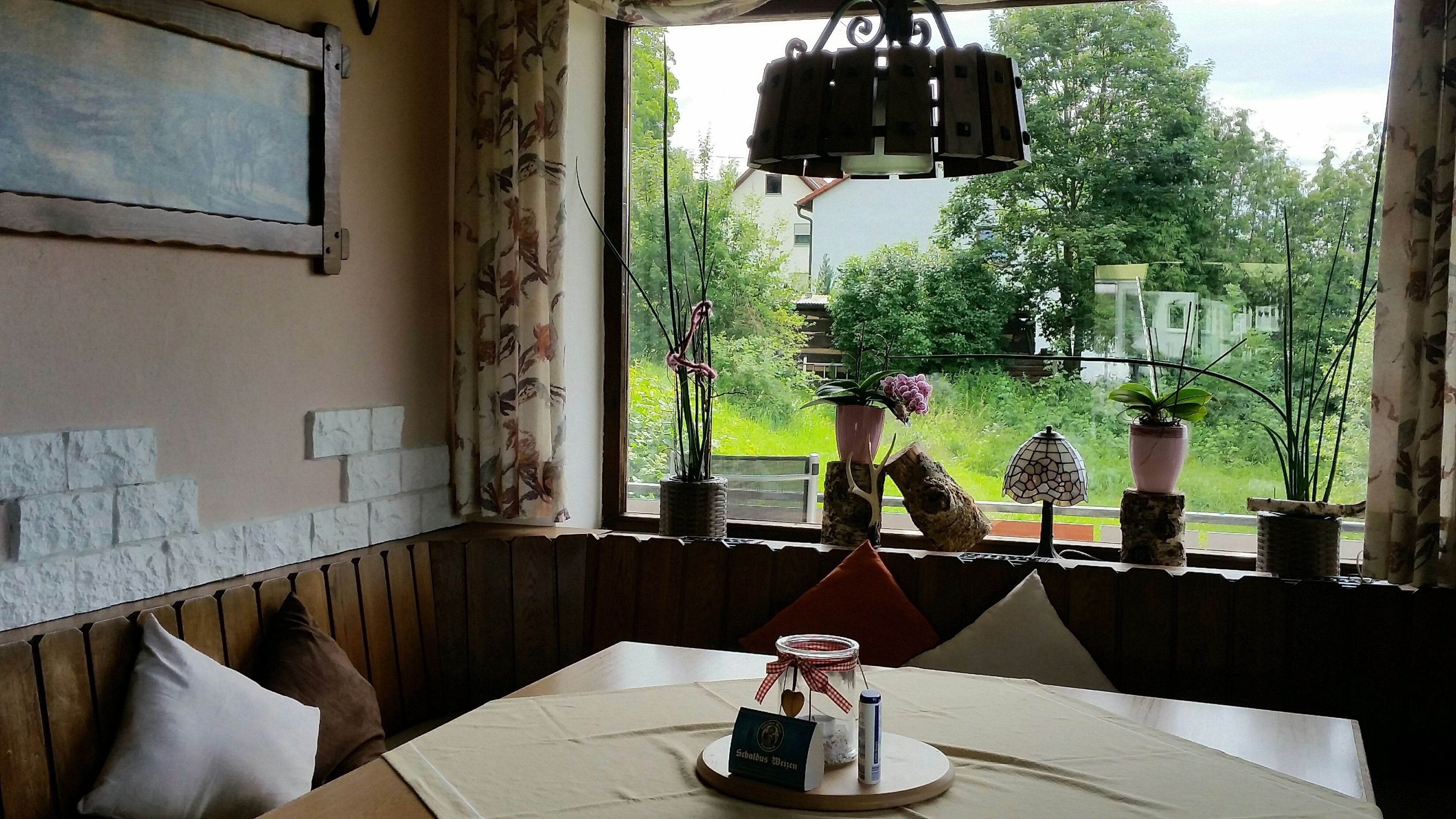 Een eethoek met een tafel voor twee personen, een raam met uitzicht op groen en een hanglamp.