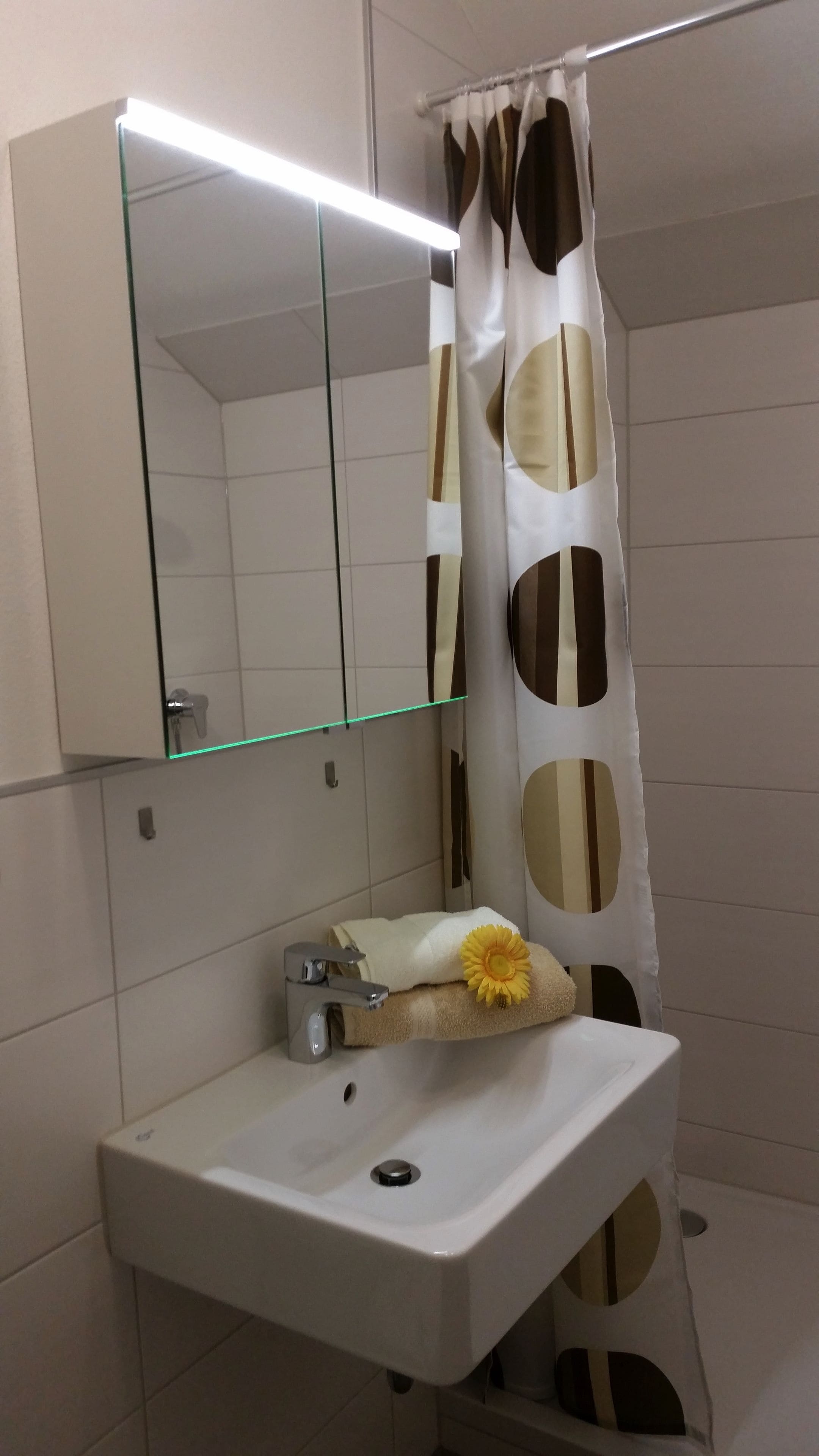 Un baño con lavamanos blanco, un espejo encima y cortina de ducha con diseño geométrico.