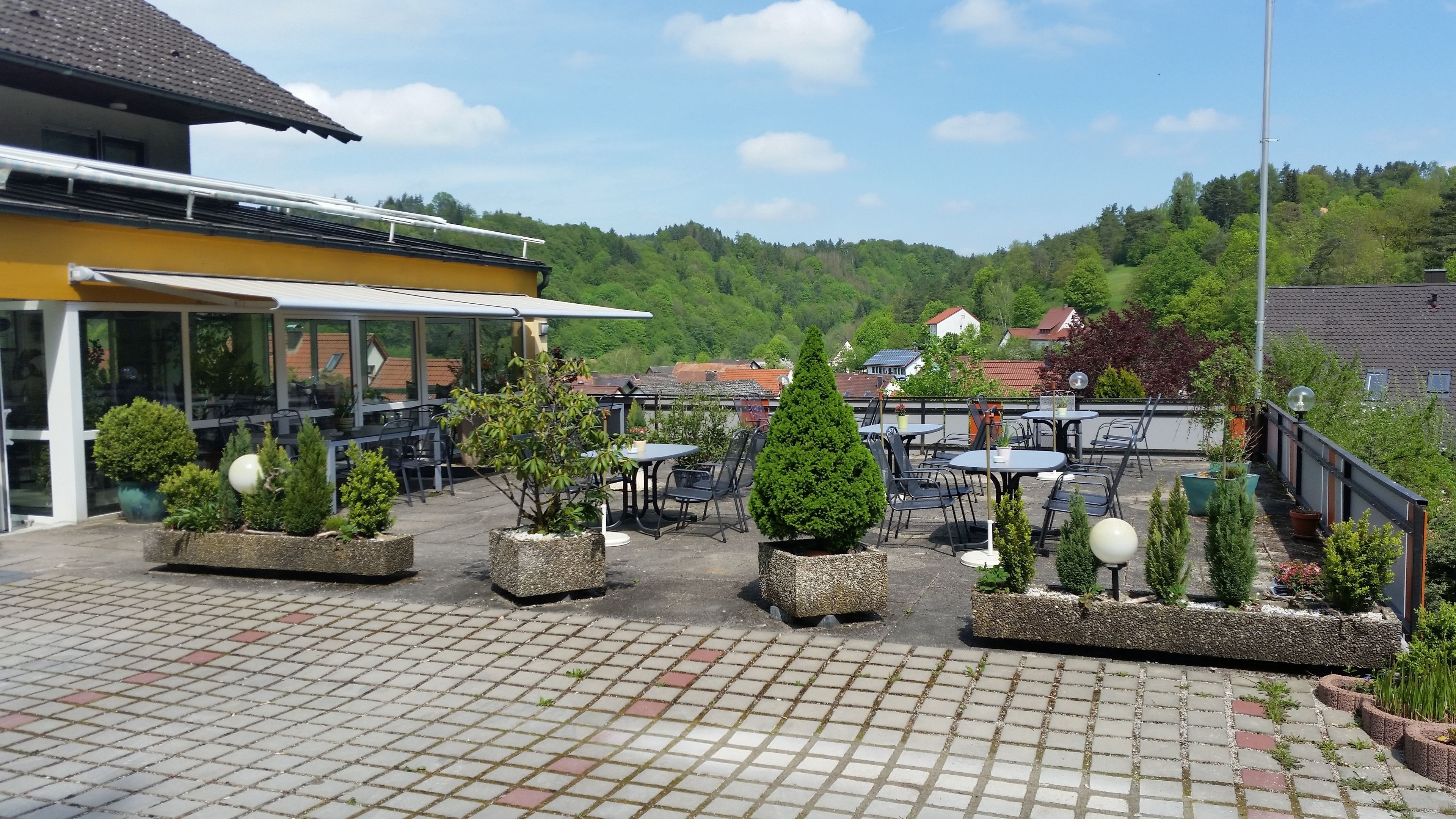 A patio area with outdoor seating, potted plants, and a view of a hillside with houses.