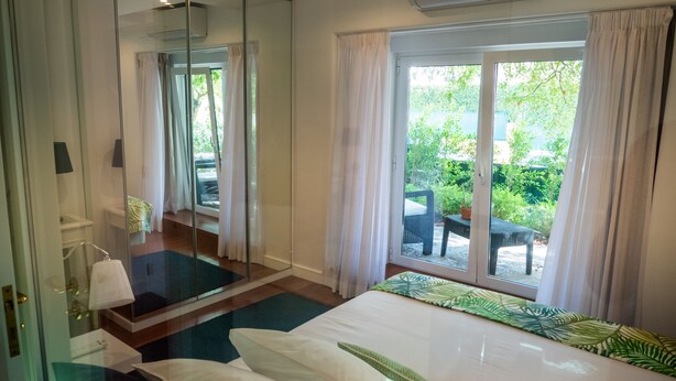 Habitación de hotel con cama, baño con espejo y vista a un jardín por una puerta corrediza.