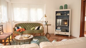 Una sala de estar con un sofá verde, una mesa de centro, una estantería y una ventana con cortinas translúcidas.