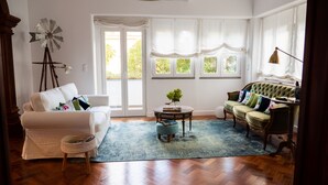 Un salón con un sofá blanco, un sillón verde, una mesa de centro redonda y una decoración con molino.