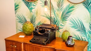 Una máquina de escribir antigua sobre un escritorio de madera, con dos jarrones verdes y una bombilla de luz al fondo.