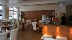 A spacious dining area with multiple tables and chairs, a central bar area, and large windows providing natural light. - Altstadthotel Rheine (Rheine)
