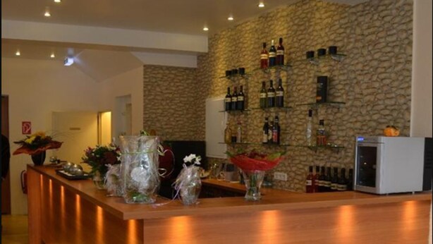 A modern kitchen with a central island, wooden stools, a stone wall, and a wine rack. - Altstadthotel Rheine (Rheine)
