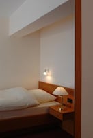 Una cama individual con cabecera de madera, una mesita de noche con lámpara y una lámpara fijada a la pared.