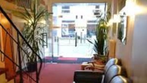 A hotel lobby with a red carpet, a black leather sofa, a staircase, and a large window. - Altstadthotel Rheine (Rheine)