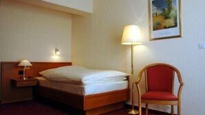 A hotel room with a bed, a nightstand, a lamp, a chair, and a painting on the wall. - Altstadthotel Rheine (Rheine)