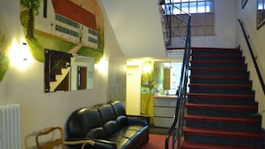 A hotel lobby with a staircase, a black leather sofa, a wooden chair, and a reception desk. - Altstadthotel Rheine (Rheine)