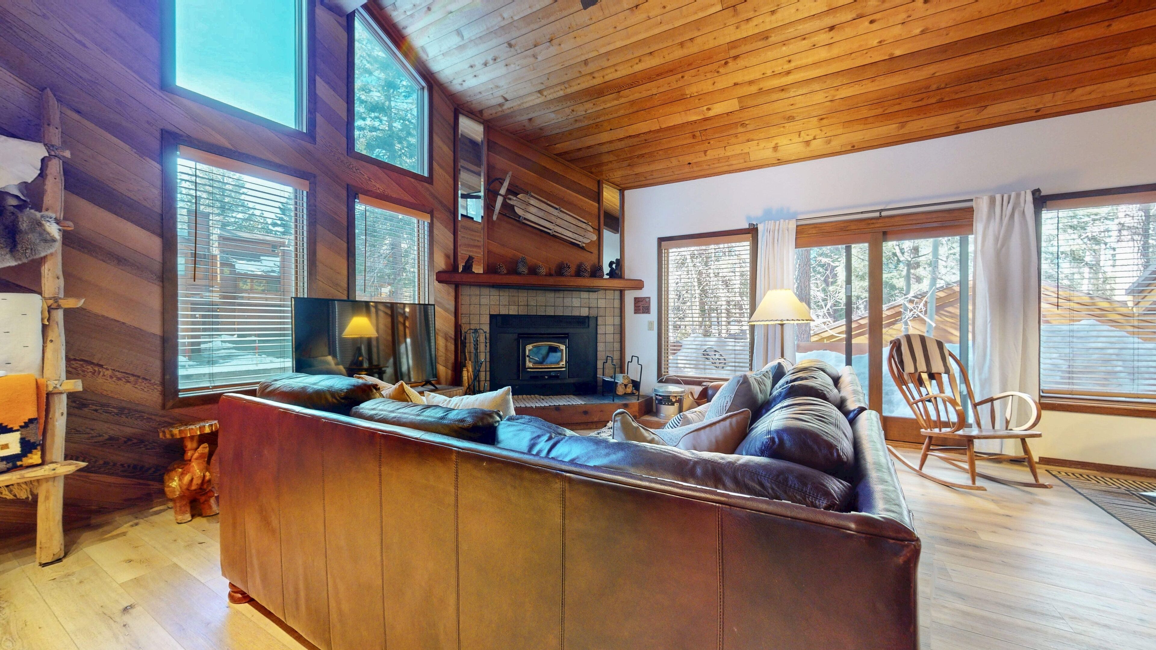 A cozy cabin interior with a wooden ceiling, a fireplace, a sofa, and a television.