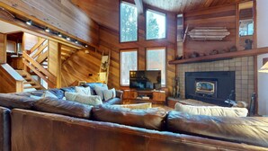 A log cabin interior with a leather sofa, a fireplace, a television, and a staircase.
