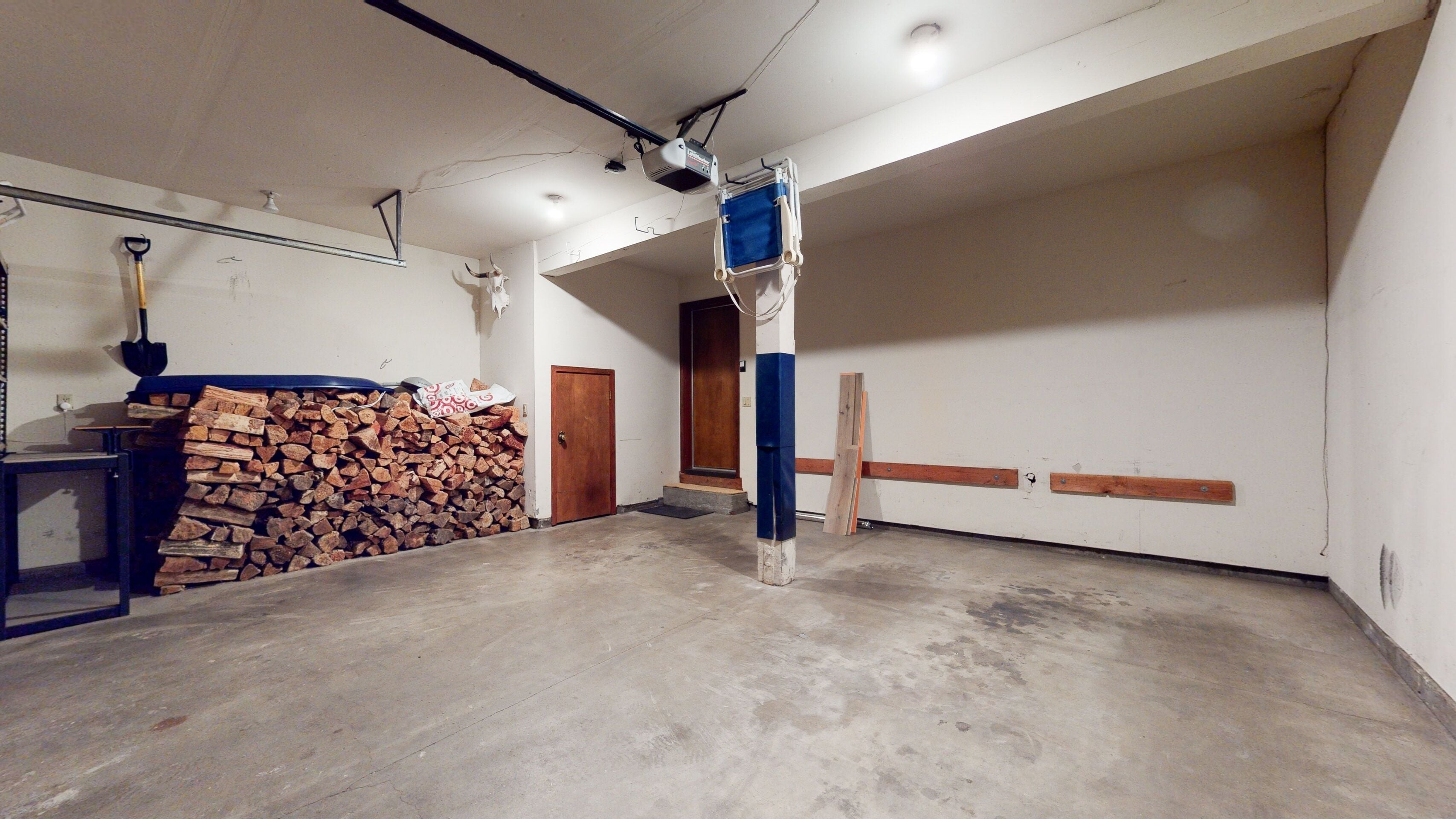 A spacious garage with a concrete floor, a wooden door, and a stack of firewood against the wall.