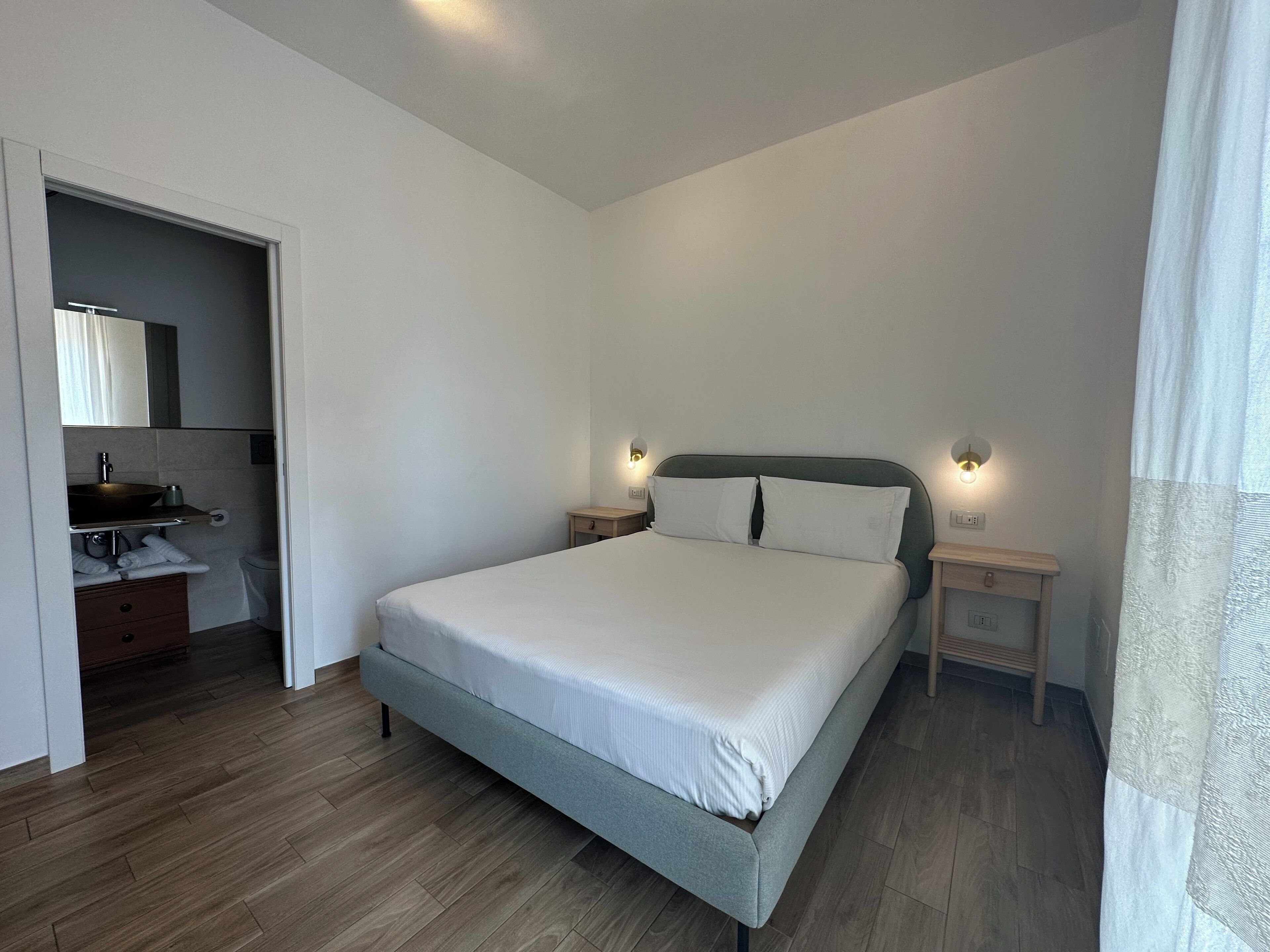A bedroom with a bed, bedside tables, a mirror, a sink, and a toilet.