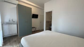 A bedroom with a bed, a wardrobe, a radiator, a TV, and a bathroom visible through an open door.