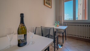 A dining area with a table set for two, a bottle of wine, and two glasses. There is a window with a view of buildings and a radiator below. - NG Guest House l'Acquedotto (Olbia)