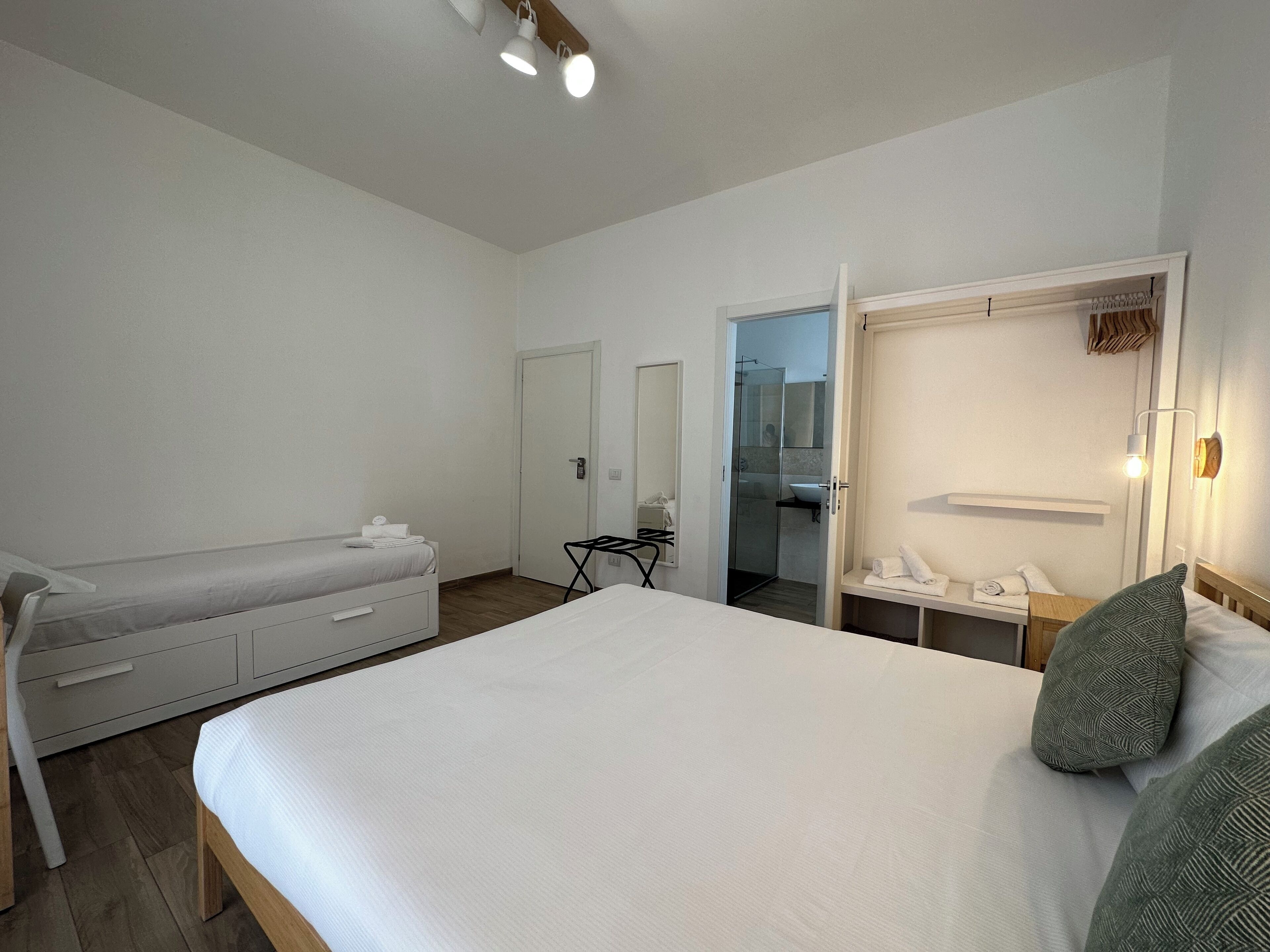 Un dormitorio con cama, cómoda, escritorio, espejo y zona de ducha.