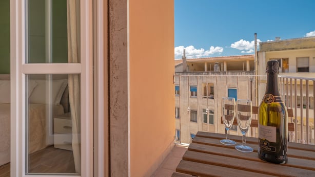 A balcony with a bottle of wine and two glasses, overlooking a cityscape. - NG Guest House l'Acquedotto (Olbia)