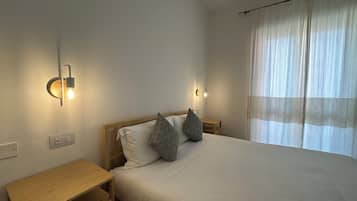 A neatly made bed with two pillows, a bedside table, and wall-mounted lights.