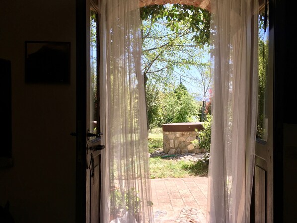 A doorway with sheer curtains, leading to an outdoor area with a stone bench and greenery. - La Fratta Art - House (Marsciano)