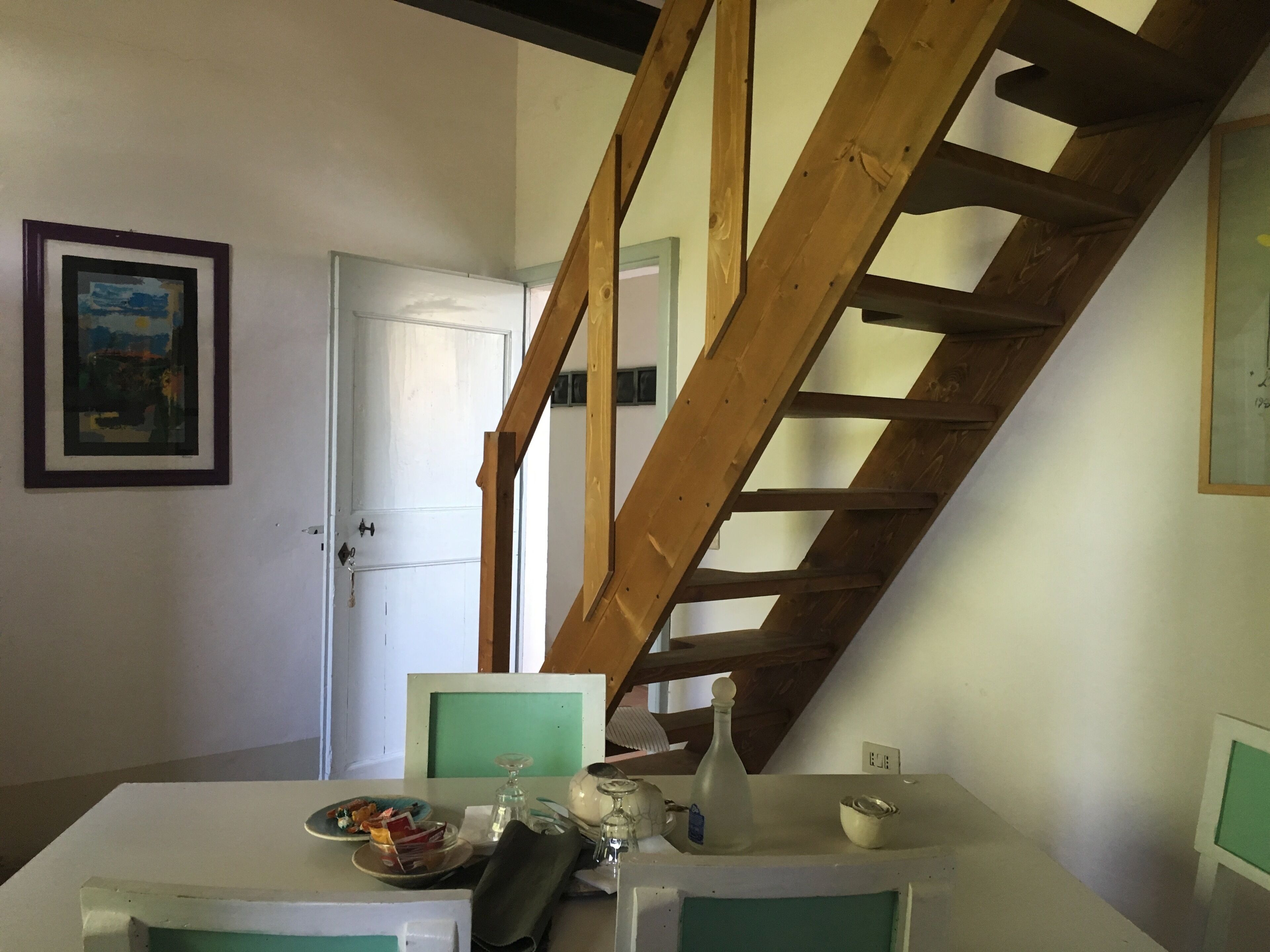 Un coin repas avec une table dressée pour deux personnes, un escalier en bois et une porte donnant sur une autre pièce.