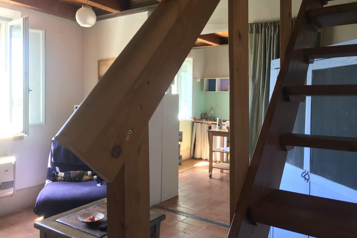 Una escalera de madera conduce a un dormitorio en un altillo con vistas a una cocina y sala de estar.