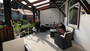 An outdoor patio area with wicker furniture, potted plants, and a view of the surrounding neighborhood. - Hotel Glück Auf (Bad Grund)