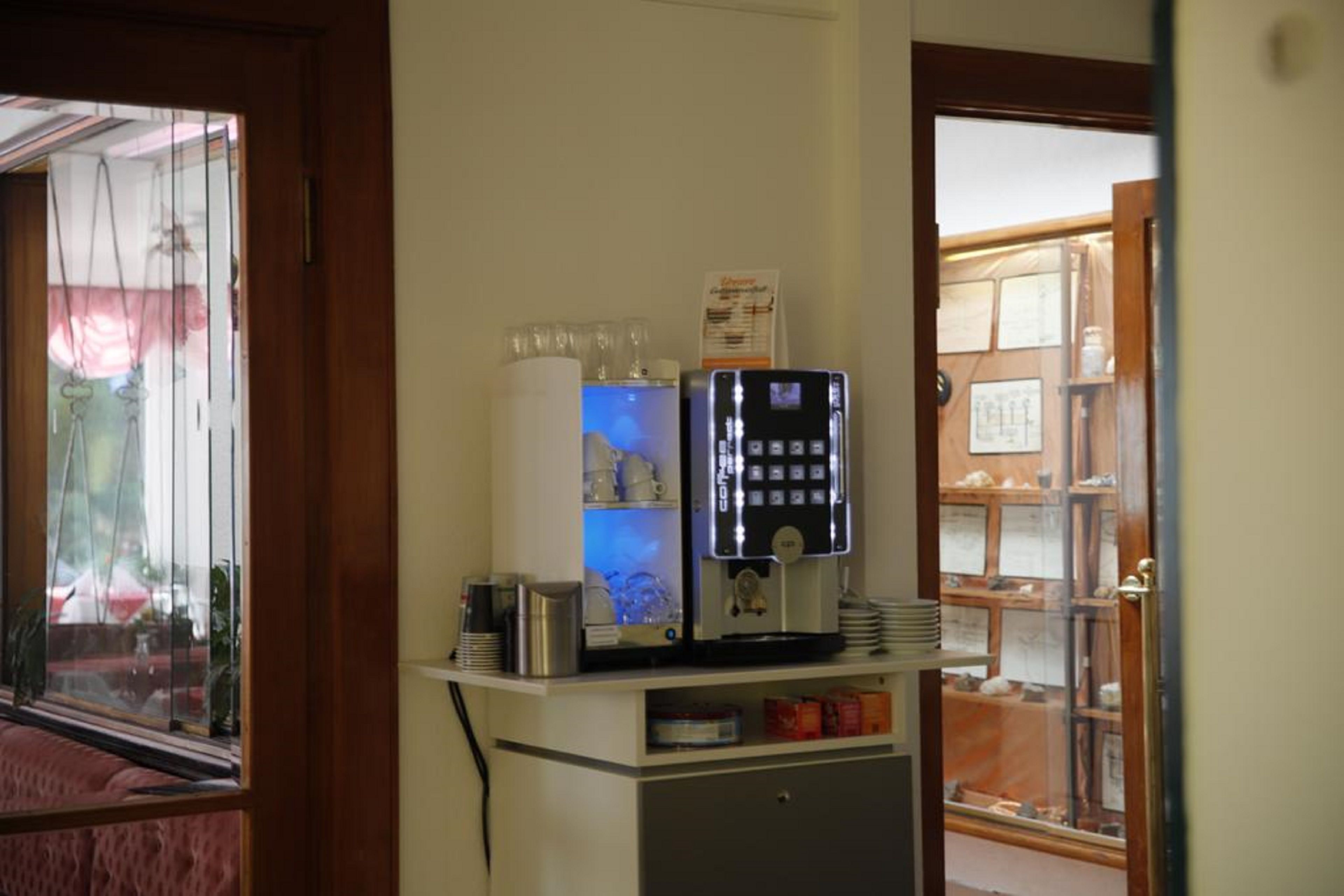 A coffee machine and a refrigerator in a room with a window and a door leading to another room.