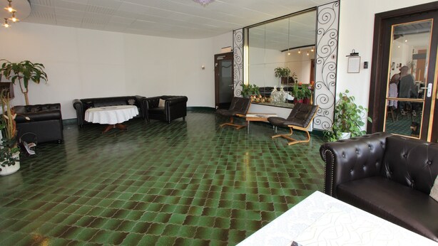 A spacious lobby with a green patterned floor, leather sofas, a dining table with a white tablecloth, and potted plants. - Hotel Glück Auf (Bad Grund)