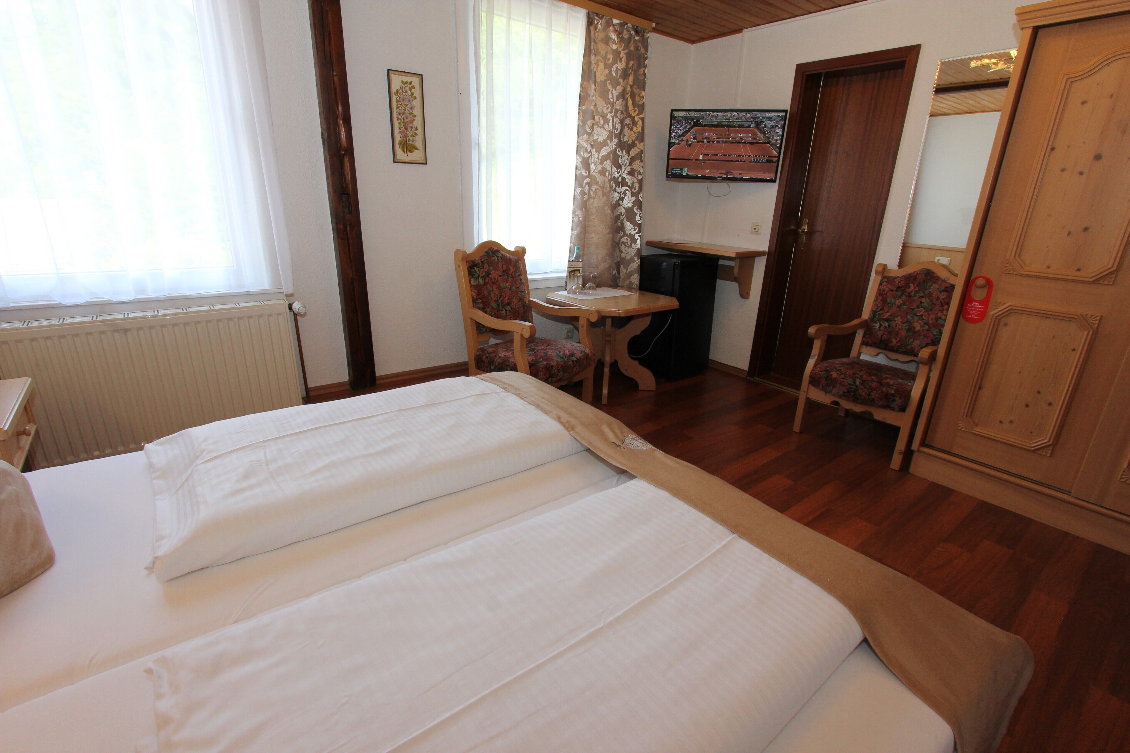 Una habitación de hotel con cama, dos sillas, una mesita, televisor y una puerta.