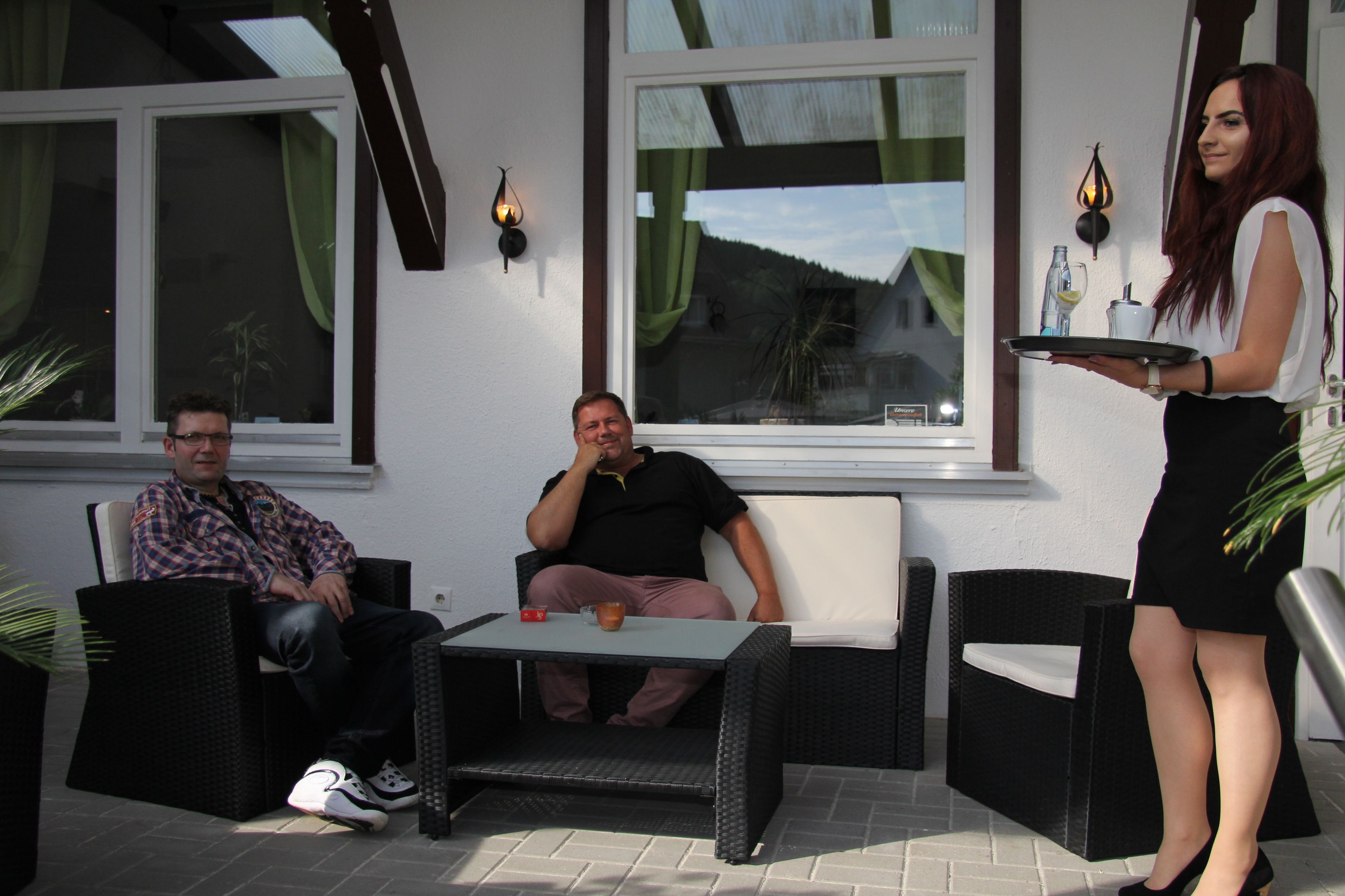 A patio area with wicker furniture, a table with a drink, and a person serving.