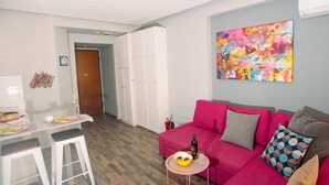 Uma sala de estar moderna com um sofá vermelho, uma mesinha redonda com uma tigela de frutas e uma garrafa, e um banquinho branco.