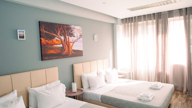 Quarto de hotel com duas camas, um quadro na parede e uma janela grande com cortinas.