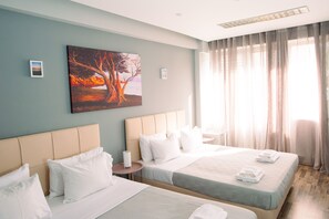 Una camera d'albergo con due letti, un quadro appeso al muro e un'ampia finestra con tende.