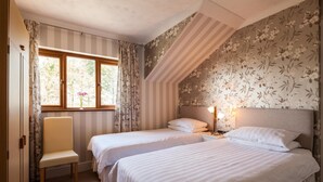 A bedroom with two beds, a window with curtains, a chair, and a nightstand with a lamp. - Langdon Farm Guest House (Kilgetty)