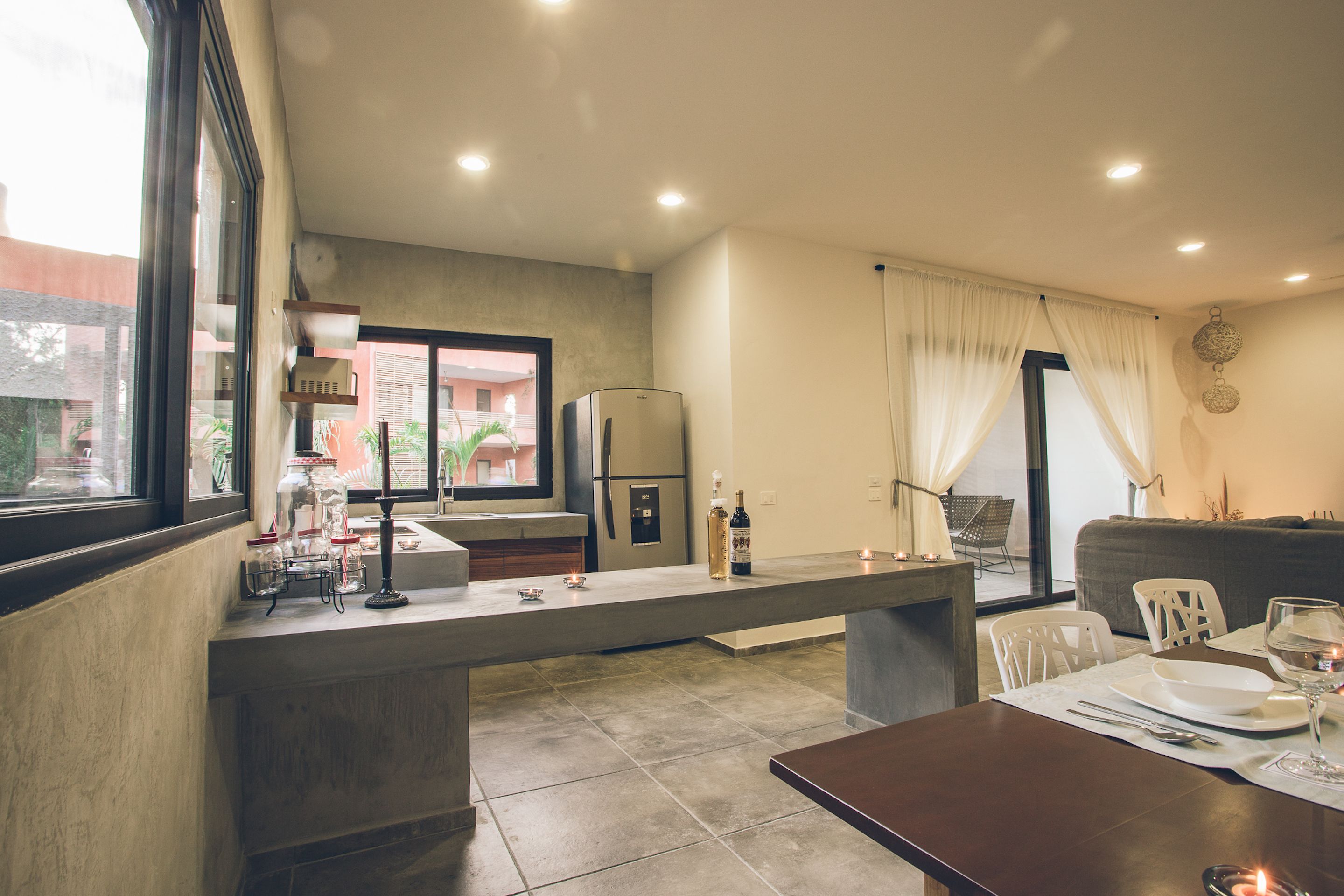 A modern kitchen with a built-in island, a dining area with a table set for two, and a view of the outside through large windows.