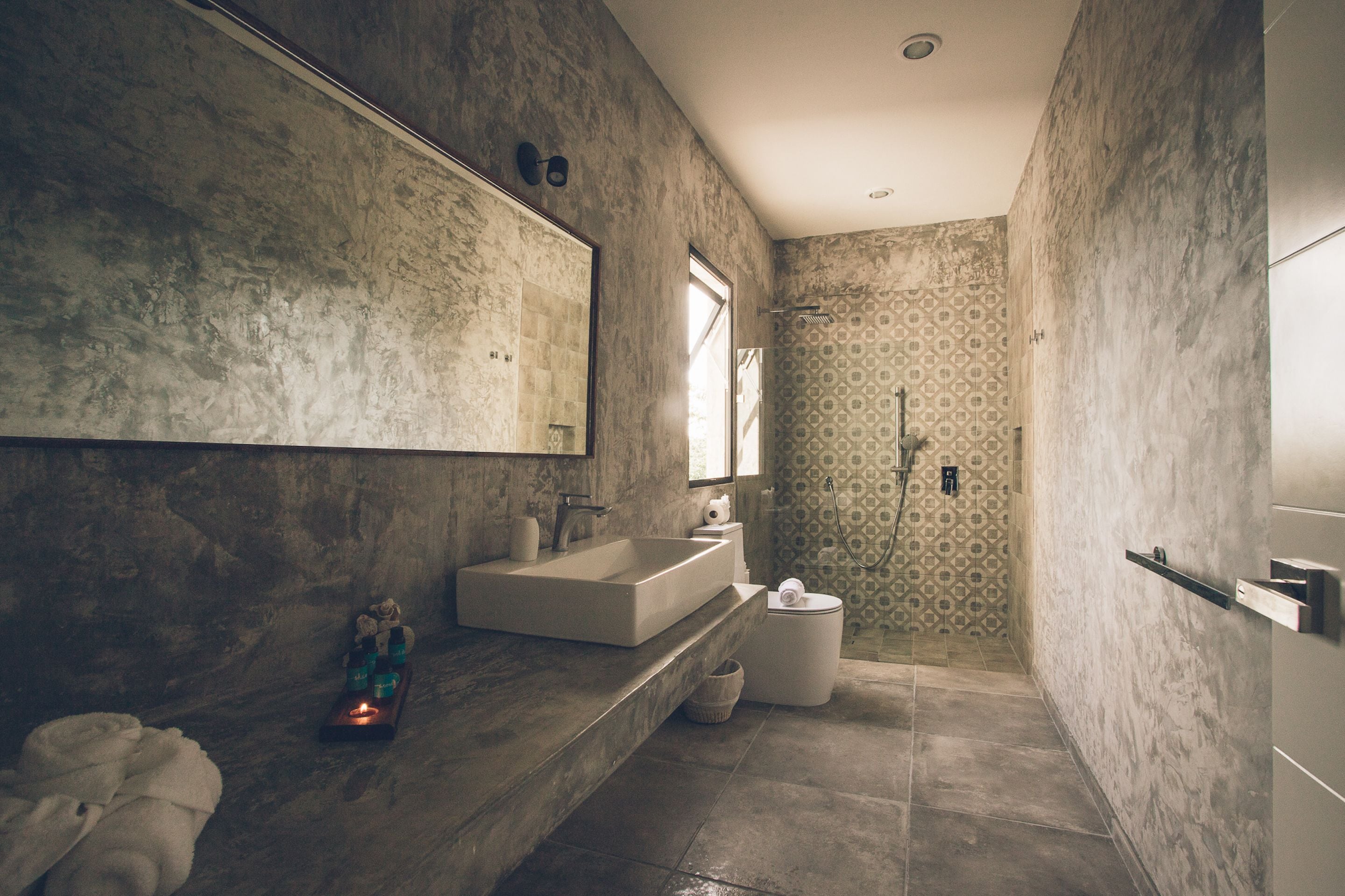 A modern bathroom with a large mirror, a rectangular sink, a shower, and a toilet.