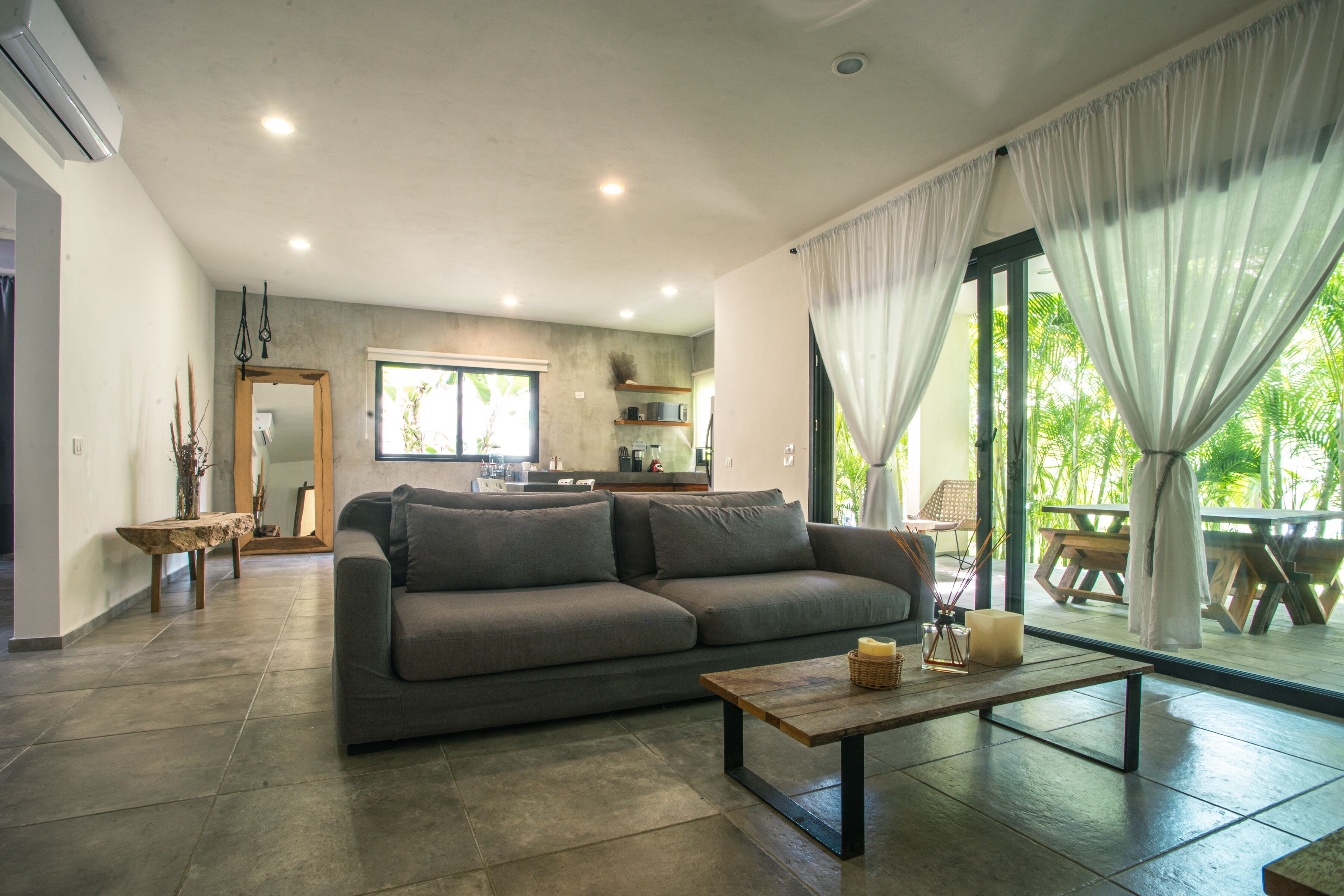 A modern living room with a grey sofa, a wooden coffee table, and a view of a patio with a table and chairs.