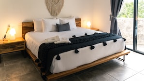 Un dormitorio moderno con una cama grande, cabecera de madera y un colgador de macramé en la pared.